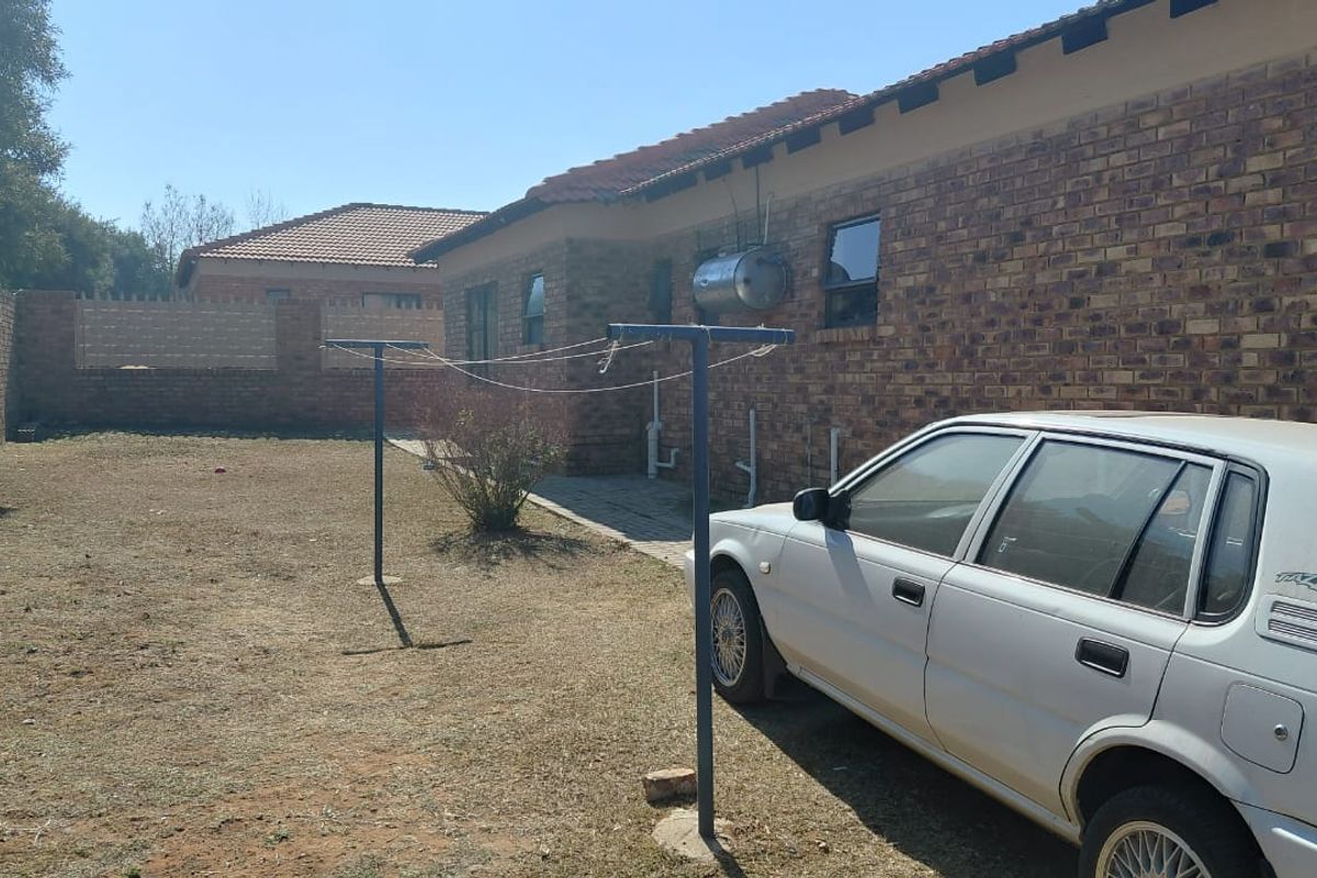 Rear exterior view of the property featuring a face brick facade, tiled roof, external geyser, and a private garden area with a paved walkway.