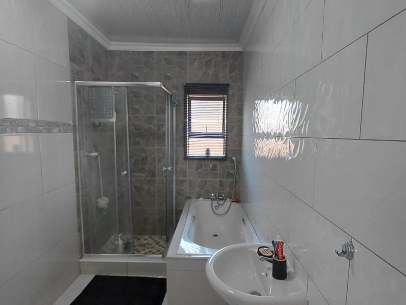 A functional bathroom featuring a glass shower enclosure, a built-in bathtub, and a pedestal basin with modern wall tiling.