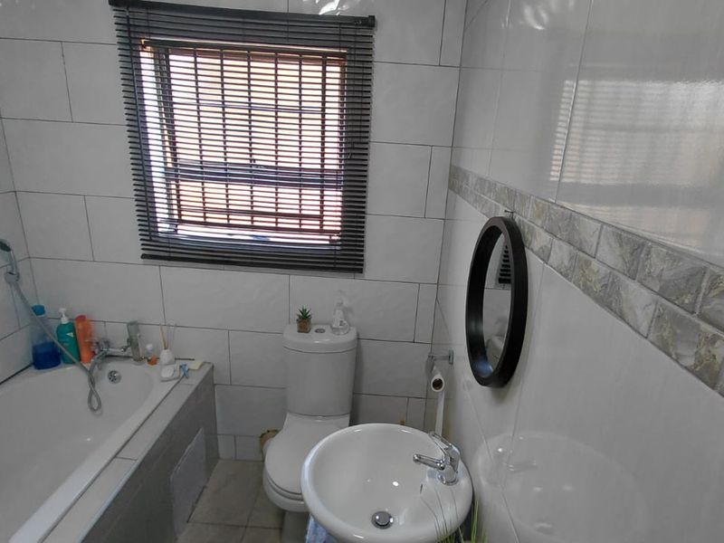 A functional bathroom featuring a bathtub with handheld shower, pedestal basin, toilet, and neutral wall tiling with a decorative border.