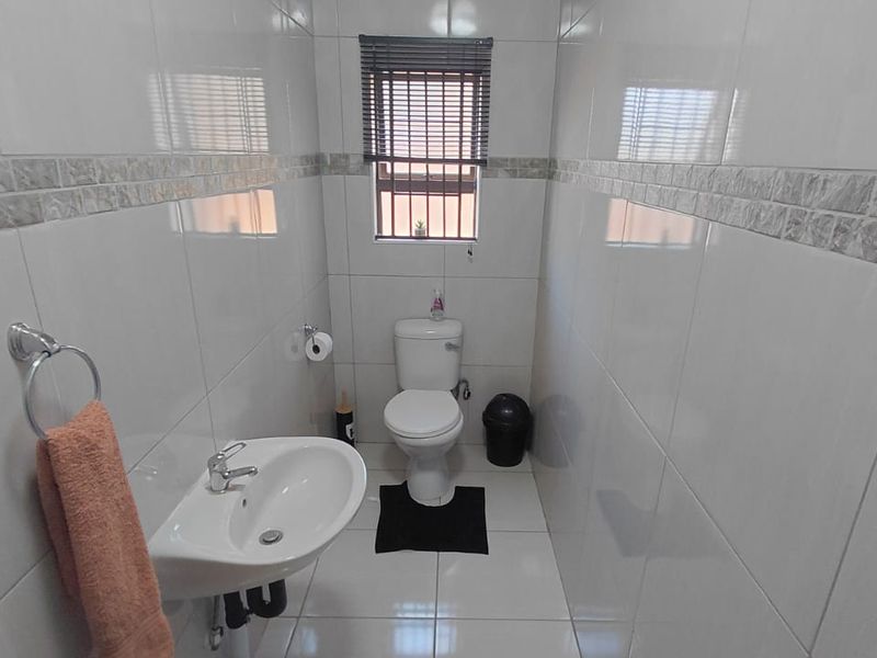 A compact, fully tiled bathroom featuring a wall-mounted basin and a standard toilet, finished with neutral ceramic tiling throughout.