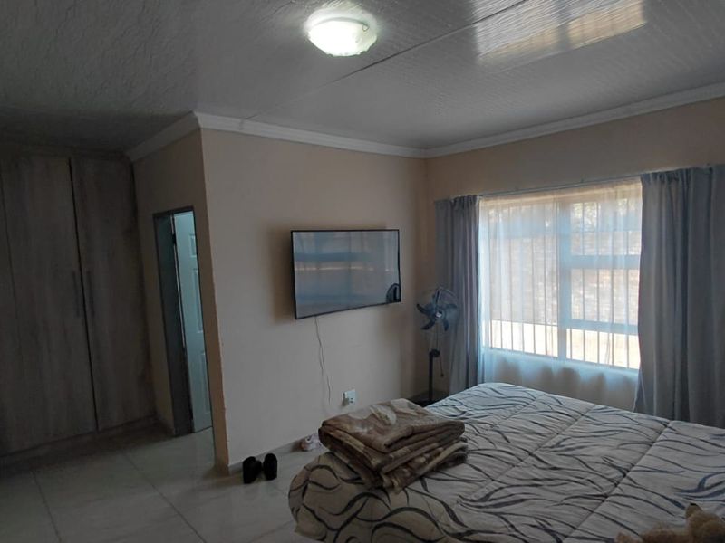 A functional bedroom featuring tiled flooring, a built-in wardrobe, and natural light through a large window.