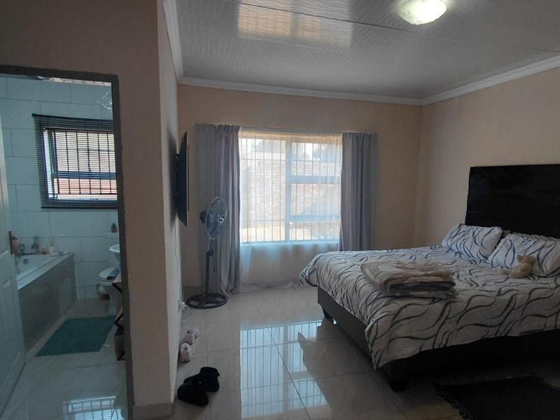 A bedroom featuring tiled flooring and an adjoining en-suite bathroom with a bathtub, offering a functional layout with natural light.