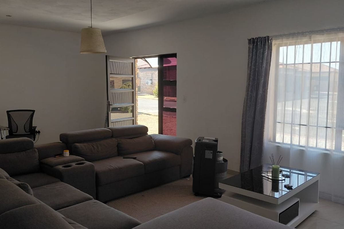 A bright living room featuring tiled flooring, a large window with natural light, and direct access to the exterior through a security gate.
