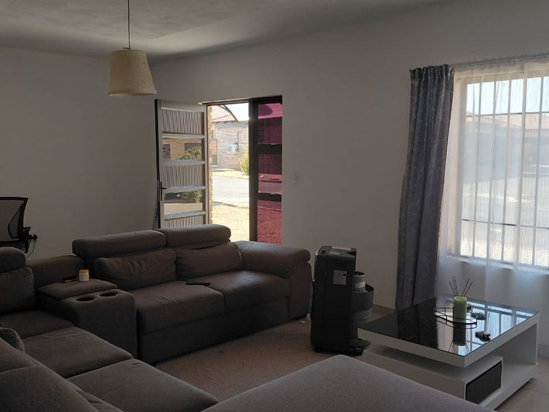 A bright living room featuring tiled flooring, a large window with natural light, and direct access to the exterior through a security gate.