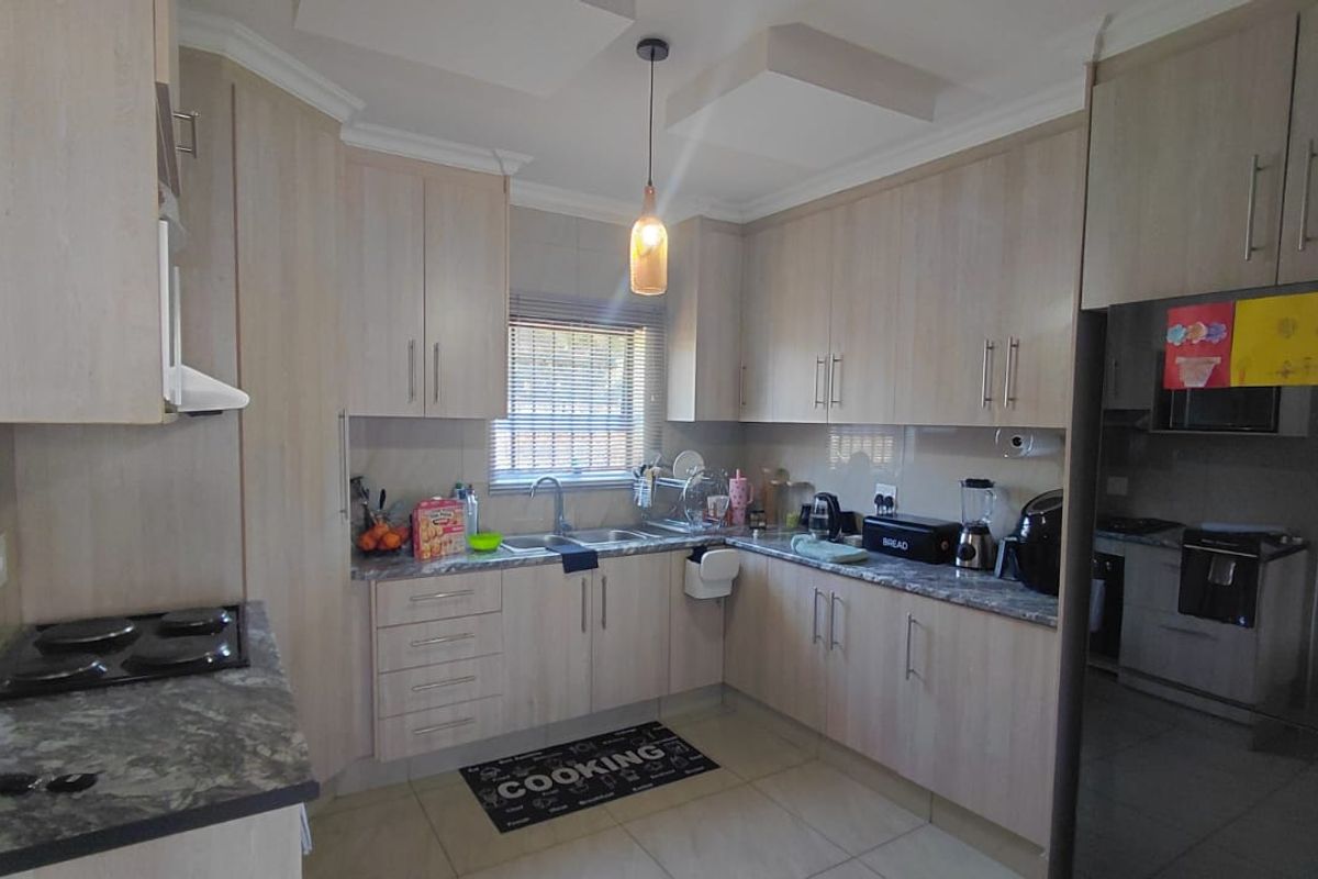 A functional kitchen featuring light wood-tone cabinetry, stone-look laminate countertops, a built-in hob, and tiled flooring with ample storage space.