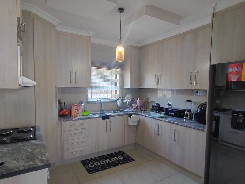 A functional kitchen featuring light wood-tone cabinetry, stone-look laminate countertops, a built-in hob, and tiled flooring with ample storage space.