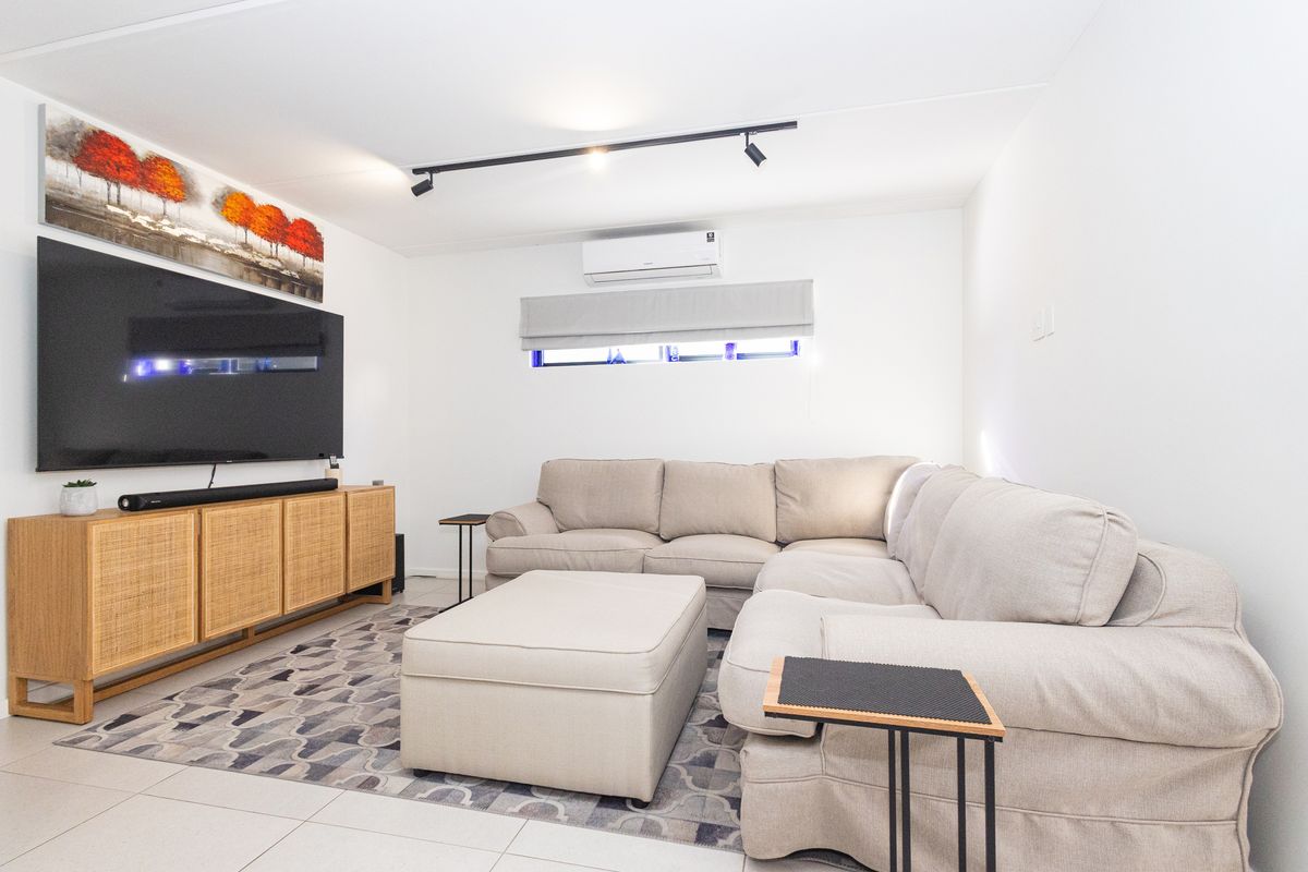 A modern living room featuring tiled flooring, track lighting, and a wall-mounted split-system air conditioner.