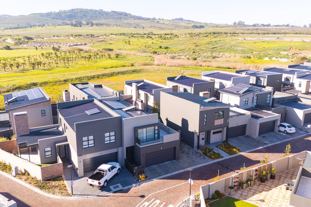 Aerial view of a modern residential estate featuring contemporary homes with solar panels, paved driveways, and landscaped surroundings.