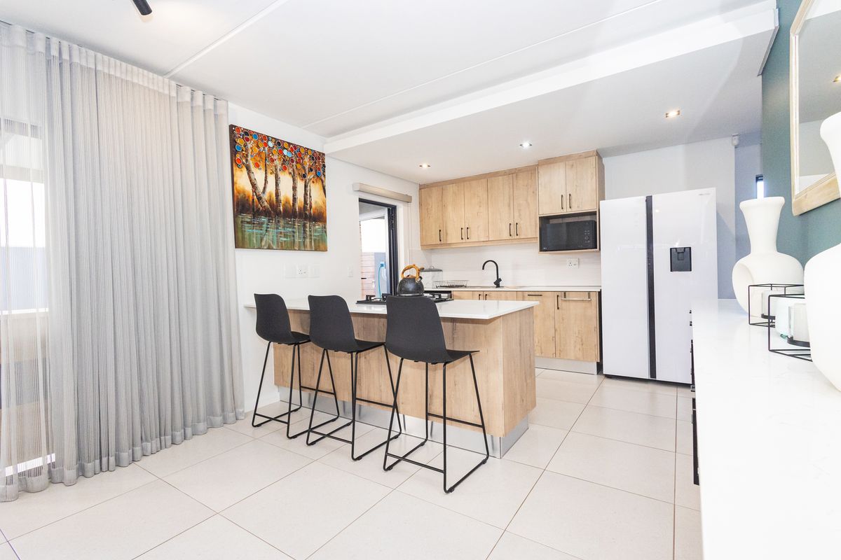 Modern kitchen featuring light wood cabinetry, stone countertops, a central island with breakfast bar seating, and sleek tiled flooring.