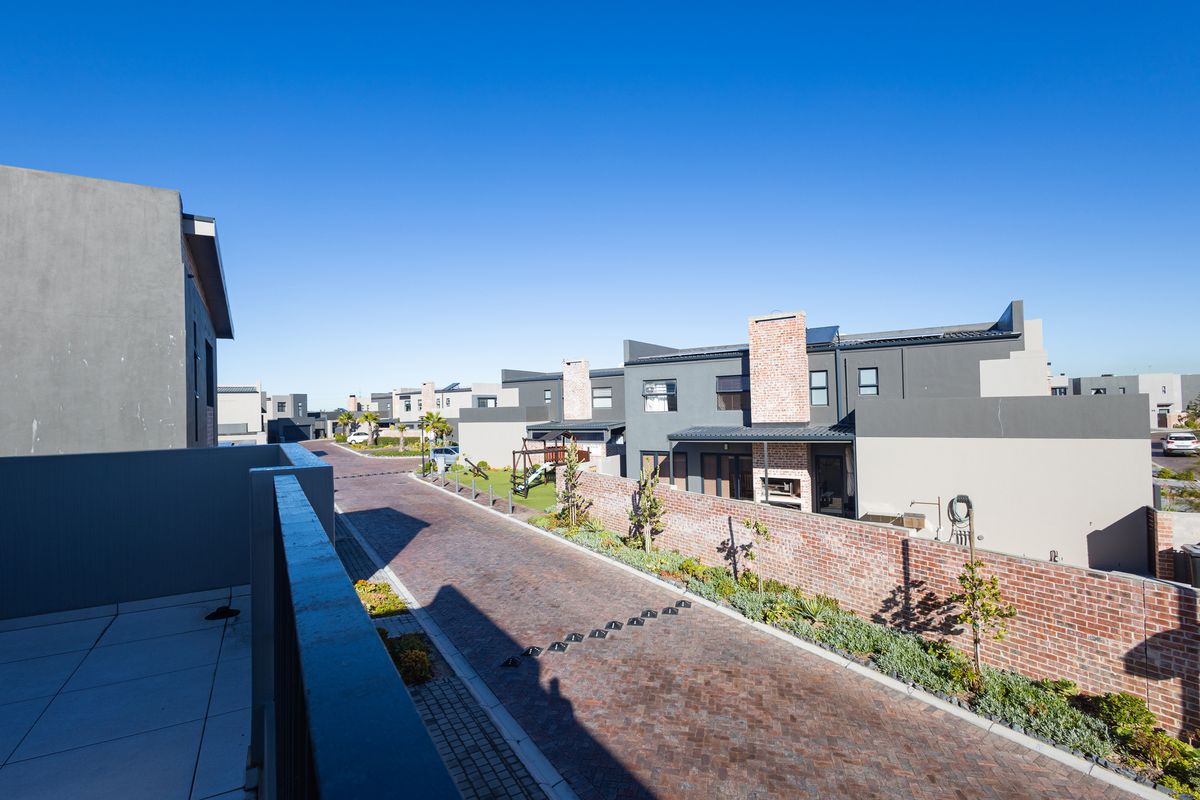 An elevated view of a modern residential complex featuring brick-paved driveways, contemporary townhouses with brick chimneys, and private balcony spaces.
