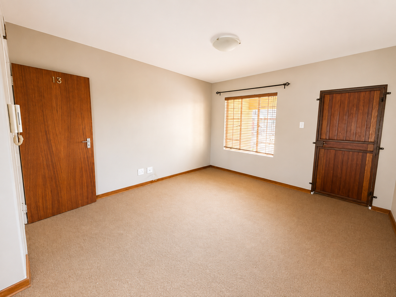 An empty bedroom featuring neutral walls, carpet flooring, a wooden entrance door, a stable-style door, and a window with fitted blinds.