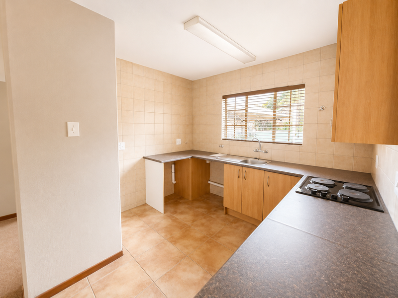 A functional, empty kitchen featuring laminate cabinetry, dark countertops, a built-in electric hob, and neutral ceramic tile finishes throughout.