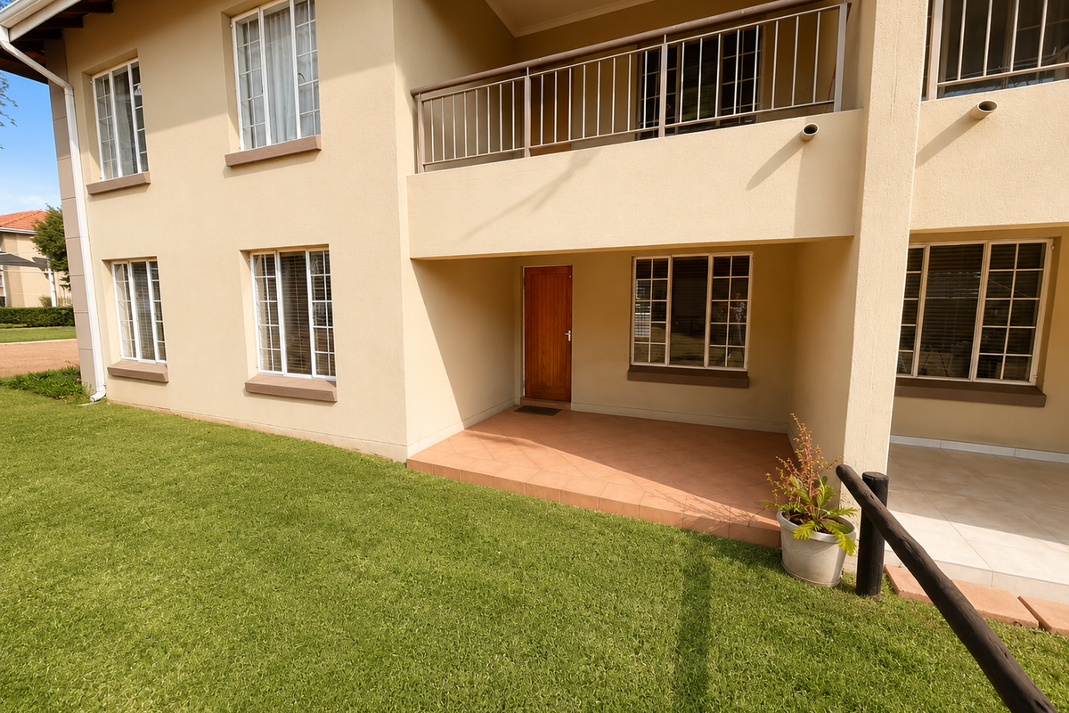 A well-maintained apartment exterior featuring a ground-floor tiled patio, a first-floor balcony with metal railings, and neat lawn area.