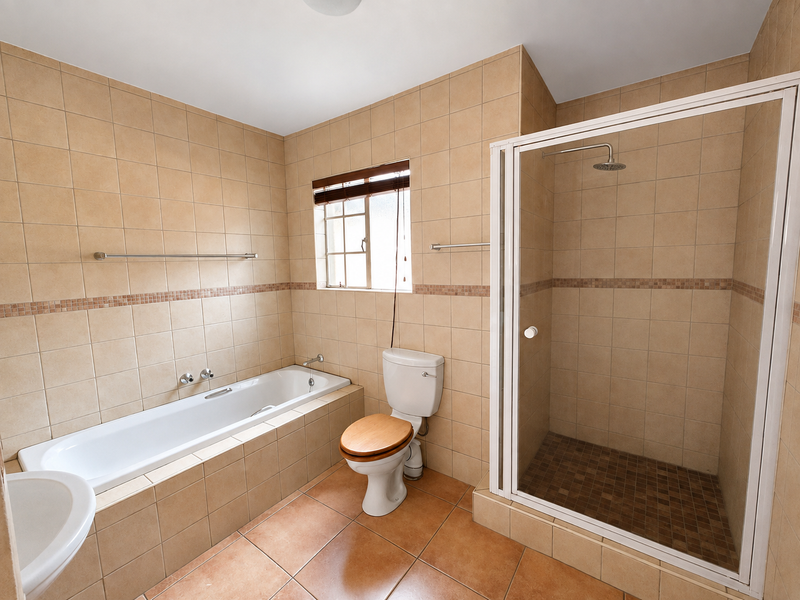 A spacious bathroom featuring a built-in bathtub, a separate shower enclosure, and neutral wall and floor tiling throughout.
