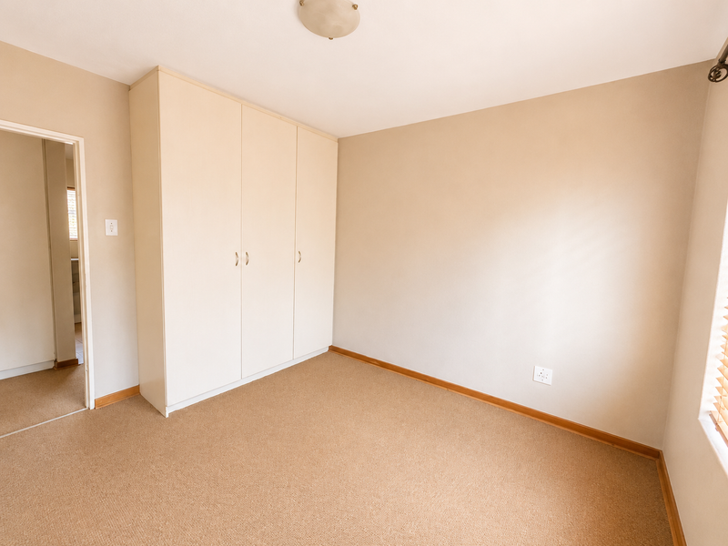 A clean, empty bedroom featuring neutral walls, carpeted flooring, and ample built-in cupboard storage space.