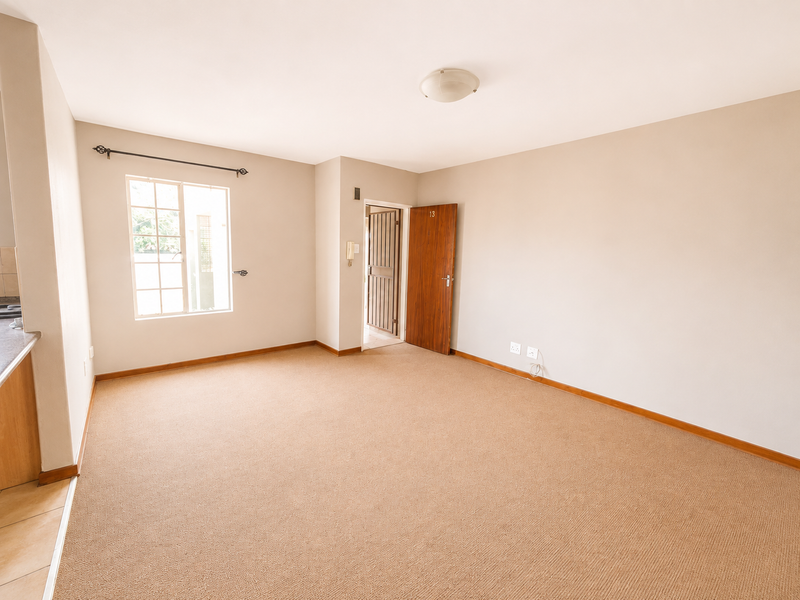 An empty, neutrally painted living room featuring carpet flooring, a timber entrance door, and an intercom system.