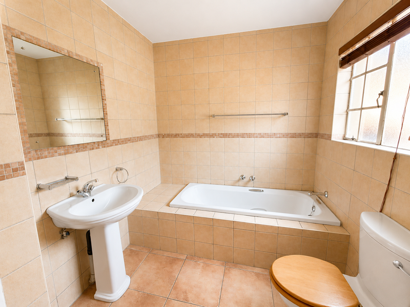 A functional bathroom featuring a built-in bathtub, pedestal basin, and neutral floor-to-ceiling tiling, offering a clean and practical space.