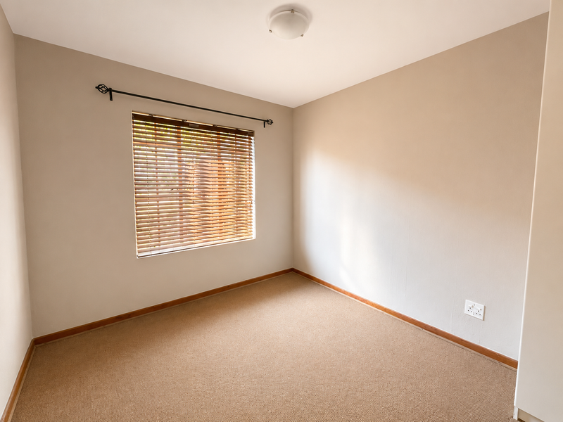 A clean, empty bedroom featuring neutral wall paint, carpeted flooring, and fitted wooden venetian blinds.