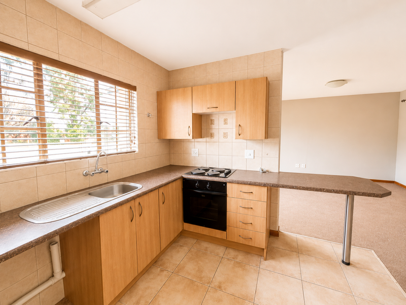 A functional kitchen featuring laminate cabinetry, built-in oven, electric hob, and a breakfast bar, seamlessly flowing into an open-plan living area.