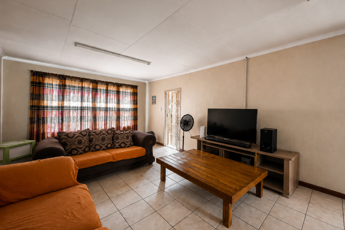 A living room featuring tiled flooring, ceiling-mounted lighting, and an external door, presenting an opportunity for cosmetic updates to improve the overall aesthetic.