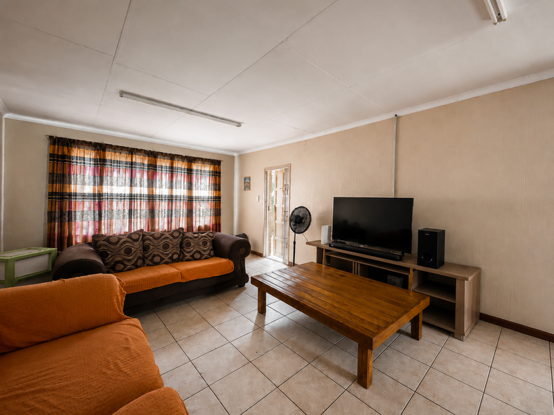A living room featuring tiled flooring, ceiling-mounted lighting, and an external door, presenting an opportunity for cosmetic updates to improve the overall aesthetic.