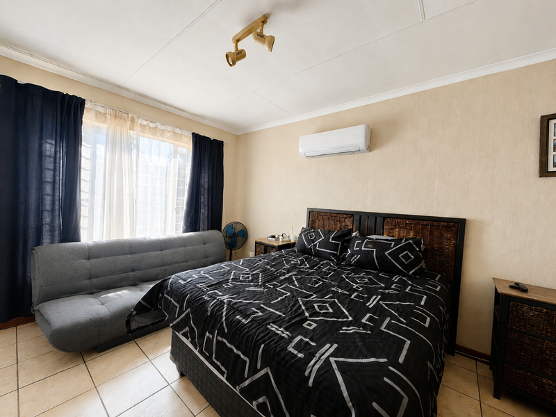 A bedroom featuring tiled flooring, a wall-mounted split-system air conditioner, and a ceiling-mounted spotlight fixture.