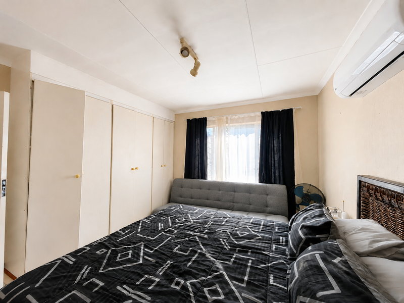 A bedroom featuring built-in cupboards, a wall-mounted split-system air conditioner, and track lighting.