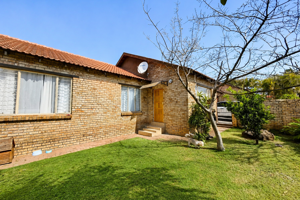 A rear view of a face brick townhouse featuring a tiled roof, a small lawn, and a paved walkway leading to the entrance.