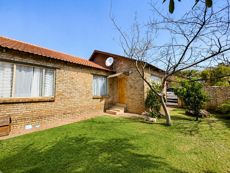 A rear view of a face brick townhouse featuring a tiled roof, a small lawn, and a paved walkway leading to the entrance.