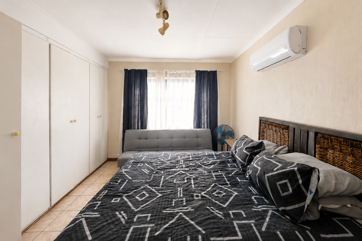A functional bedroom featuring built-in cupboards, tiled flooring, and a wall-mounted air conditioning unit.
