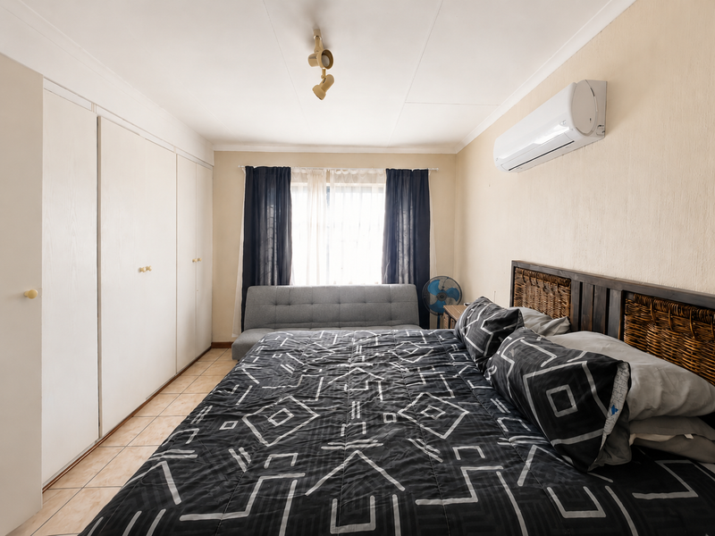 A functional bedroom featuring built-in cupboards, tiled flooring, and a wall-mounted air conditioning unit.