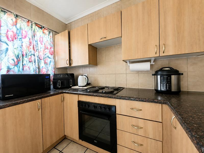 A functional kitchen featuring light wood-finish cabinetry, dark granite-look countertops, a built-in electric oven with hob, and neutral ceramic wall and floor tiling.
