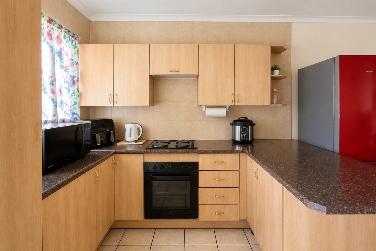 A functional U-shaped kitchen featuring light wood-tone cabinetry, dark laminate countertops, a built-in oven, electric hob, and neutral tiled flooring.
