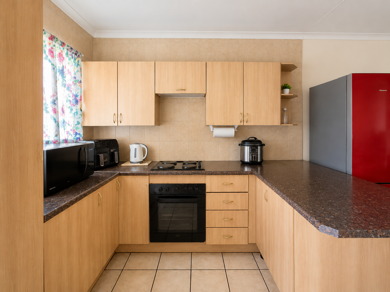 A functional U-shaped kitchen featuring light wood-tone cabinetry, dark laminate countertops, a built-in oven, electric hob, and neutral tiled flooring.