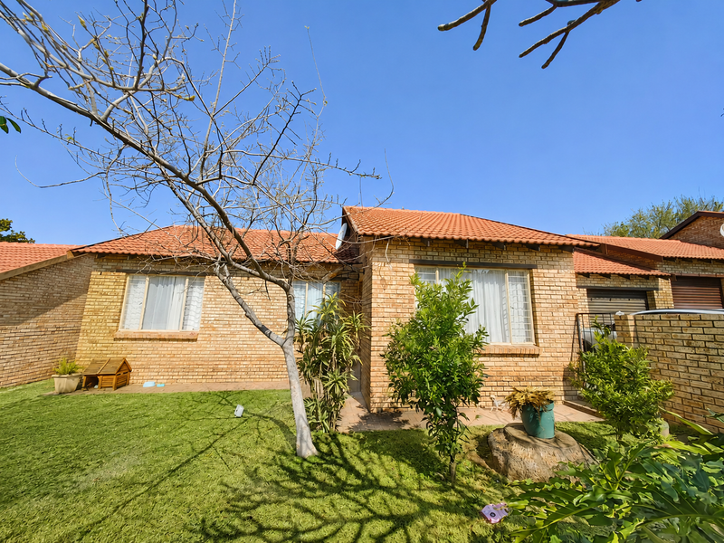 Rear view of a face brick townhouse featuring a paved patio, well-maintained lawn, and terracotta tiled roof.