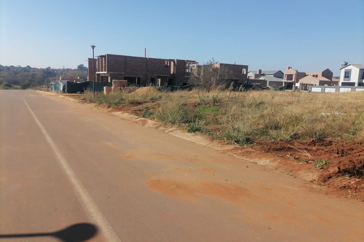 A street-level view of a vacant residential plot in a developing estate with surrounding construction activity.