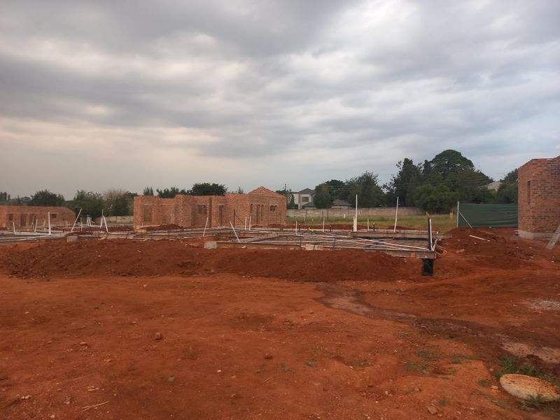 A residential construction site showing brick walls and concrete foundations with plumbing rough-ins, currently in the early stages of development.