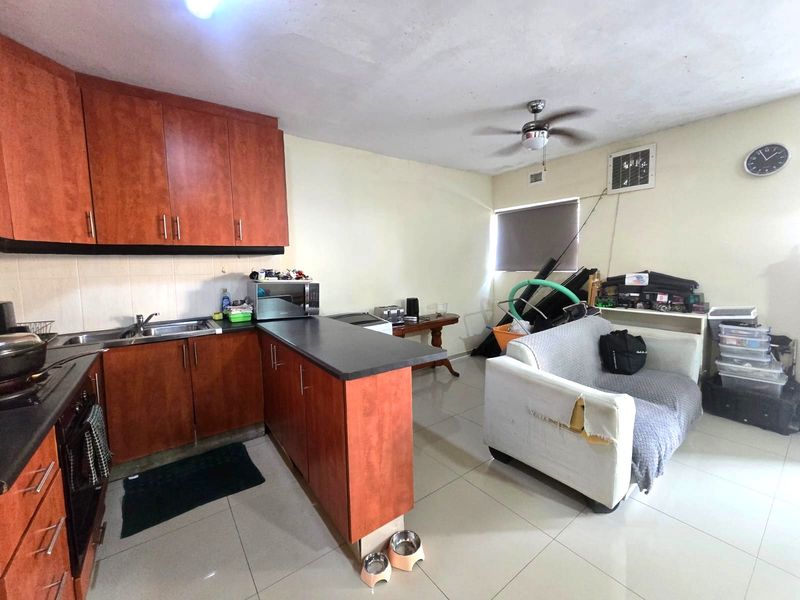 Open plan kitchen and living area featuring wood-look cabinetry, tiled flooring, and a ceiling fan, offering a functional layout with potential for cosmetic updates.