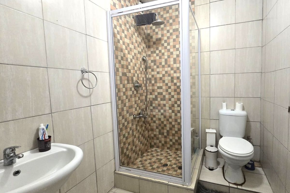 A functional bathroom featuring a tiled shower enclosure, pedestal basin, and toilet with neutral wall and floor tiling.