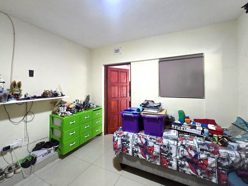 A bedroom featuring tiled flooring, a timber door, and a roller blind, currently used as a storage and hobby space.