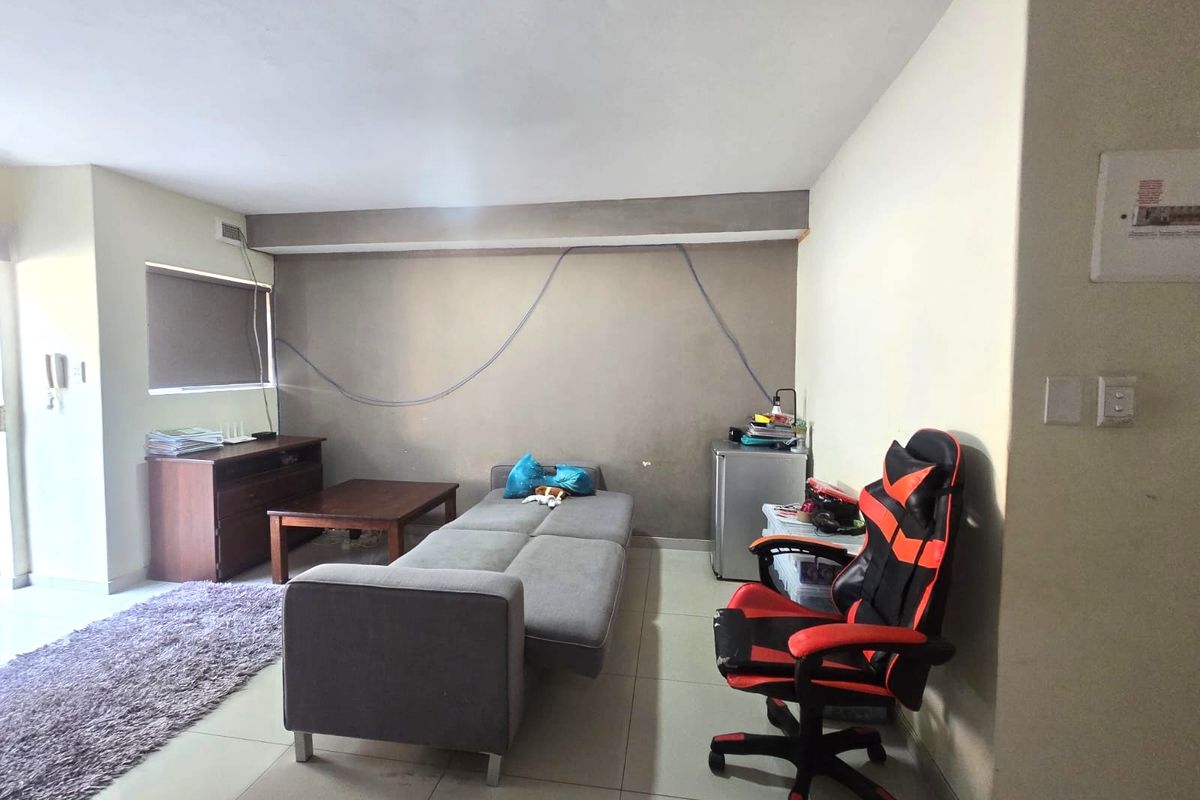 A living room area featuring tiled flooring and a roller blind, currently showing signs of wear including exposed wall wiring and scuffed paint.