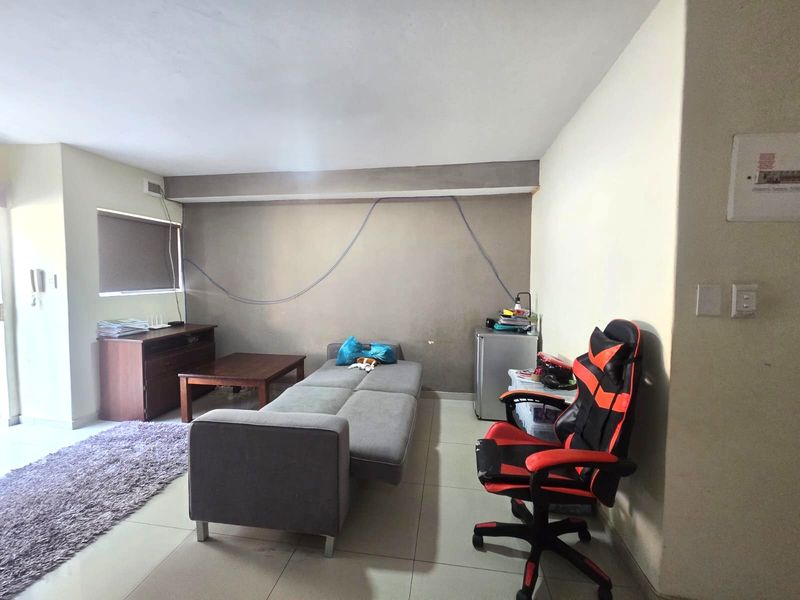 A living room area featuring tiled flooring and a roller blind, currently showing signs of wear including exposed wall wiring and scuffed paint.