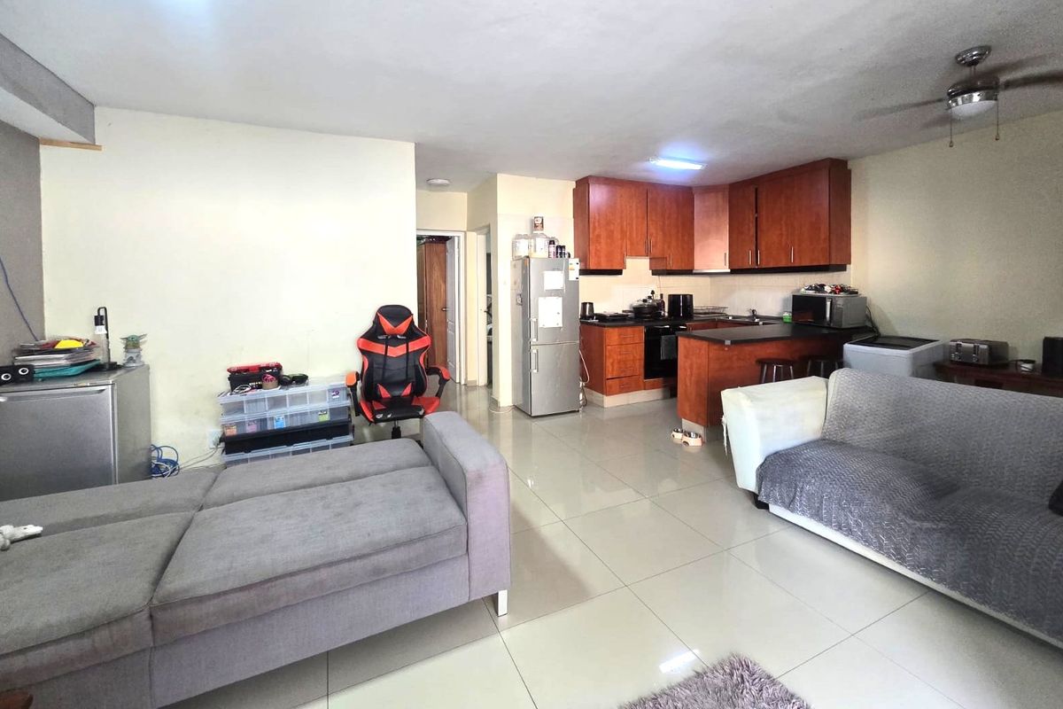 Open-plan living area featuring a functional kitchen with wood-finish cabinetry, tiled flooring throughout, and a ceiling fan in the living space.