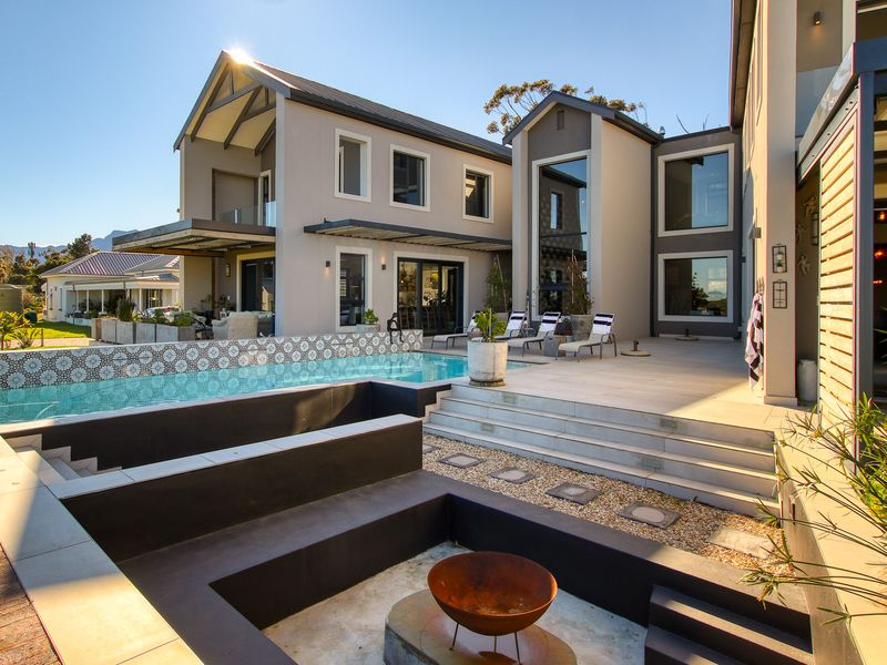 A modern rear exterior featuring a swimming pool, a sunken fire pit area, and a spacious tiled patio with contemporary architectural design.
