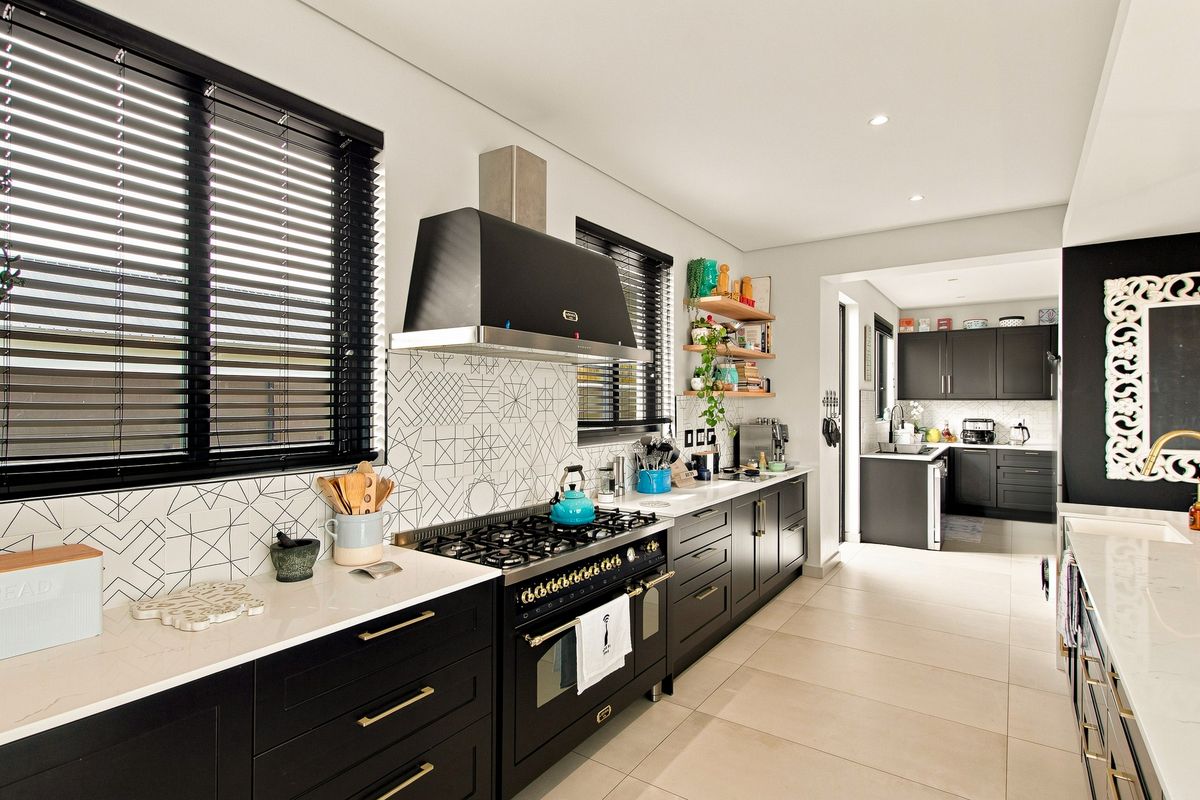 Modern kitchen featuring dark cabinetry, stone countertops, a gas range with extractor hood, and a geometric tiled backsplash, with an adjoining scullery area.