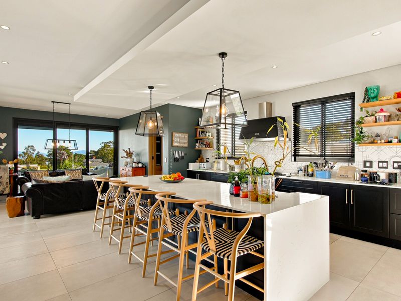Modern open-plan kitchen and living area featuring a large central island, sleek cabinetry, stone countertops, and expansive sliding doors leading to an outdoor view.