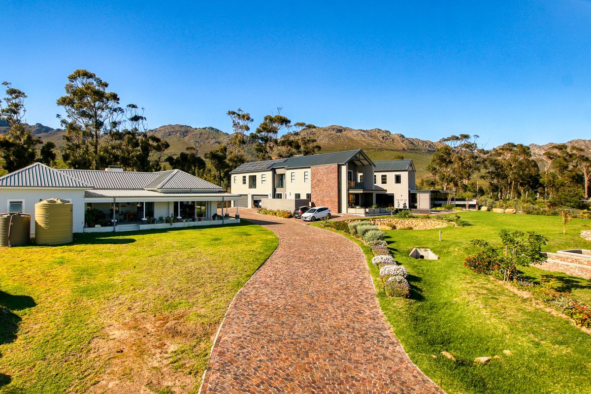 Aerial view of a large residential property featuring a cobblestone driveway, expansive lawns, and modern multi-structure architecture set against a mountain backdrop.