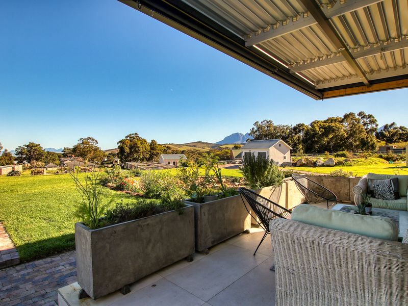 A covered patio featuring tiled flooring and concrete planters, offering expansive views of the landscaped garden and surrounding mountain landscape.