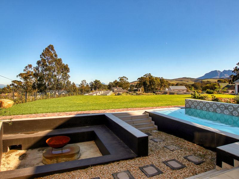 Outdoor entertainment area featuring a modern swimming pool with a tiled water feature and a sunken fire pit overlooking a spacious landscaped garden.