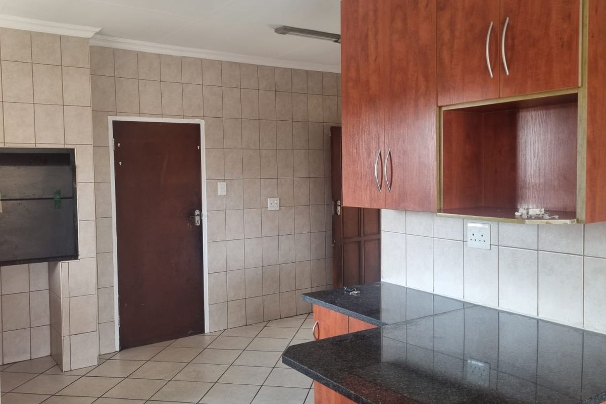 A functional kitchen featuring built-in cabinetry, granite countertops, tiled walls, and a built-in indoor braai area.